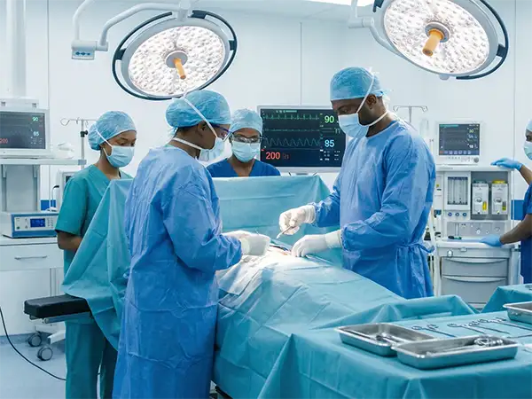 Suggested Alt Text: "A photorealistic, 4K image of a surgical team of five Black medical professionals in a state-of-the-art operating room. The surgeons and nurses, wearing blue and teal scrubs, surgical caps, and masks, are intensely focused on a procedure at the operating table. The sterile, modern environment is equipped with high-tech monitoring screens displaying vitals and large, bright overhead surgical lights, representing advanced general surgery care.